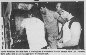 Black and white photograph of video game players with caption: "Vinnie Mancuso tries his hand at video game at Rutherford's Great Escape while Lou Giordano, John Matino and arcade manager Dave Weinman watch.