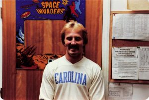 Store manager Dennis Moore poses in front of a Space Invaders bezel inside the office of Barrel of Fun #06 in Lenoir Mall, Lenoir, NC circa 1980