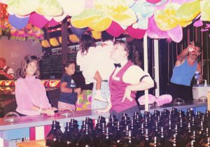 Customers and attendant underneath plush prizes at Ring Toss game at Barrel of Fun #13, Commander Ragtime's