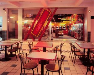 Tables and chairs sit outside the Time-Out arcade entrance with red, tilted sign and games visible inside the arcade