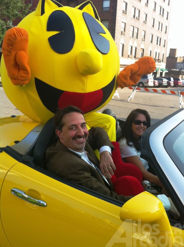 David Bishop riding in a yellow convertible with a Pac-Man mascot and female driver wearing sunglasses
