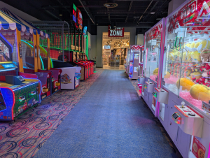 Round1 arcade aisle with plush-filled claw machines on the right and arcade games on the left, leading to Victory Zone shop