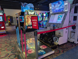 Round1 arcade floor with a roped-off DanceDance Revolution dance pad and a red sign reading "Watch your step