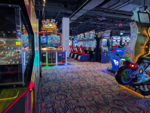 Arcade floor with racing cabinets, a Minecraft Dungeons Arcade card machine, and a Raw Thrills Snowboarder ride