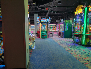 Arcade floor lined with brightly lit claw machines, including Mickey and Friends and Godzilla Kaiju Drop games