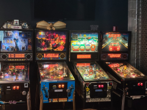 Four pinball machines in a row in an arcade: The Addams Family, Judge Dredd, South Park, and The Getaway: High Speed II