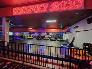 Bumper car arena under a glowing red neon "BUMPER CARS" sign, with colorful cars on a disco-lit floor and a "Spin Zone" backdrop