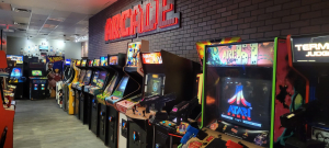 Rows of classic arcade cabinets, including Atari's Area 51 and X-Men, under a red neon ARCADE sign