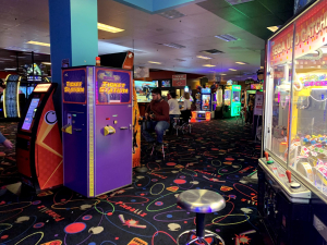 Arcade floor with a purple Ticket Station machine, a Sega UFO Catcher claw machine, and a player seated at a game