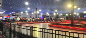 Indoor go-kart track with red-lit barriers and a black railing, with arcade games along the back wall